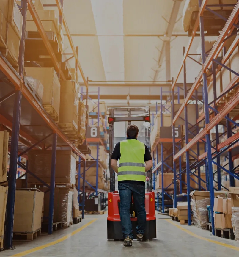 A large warehouse filled with neatly stacked boxes and pallets. Forklifts are moving around, transporting goods for distribution.