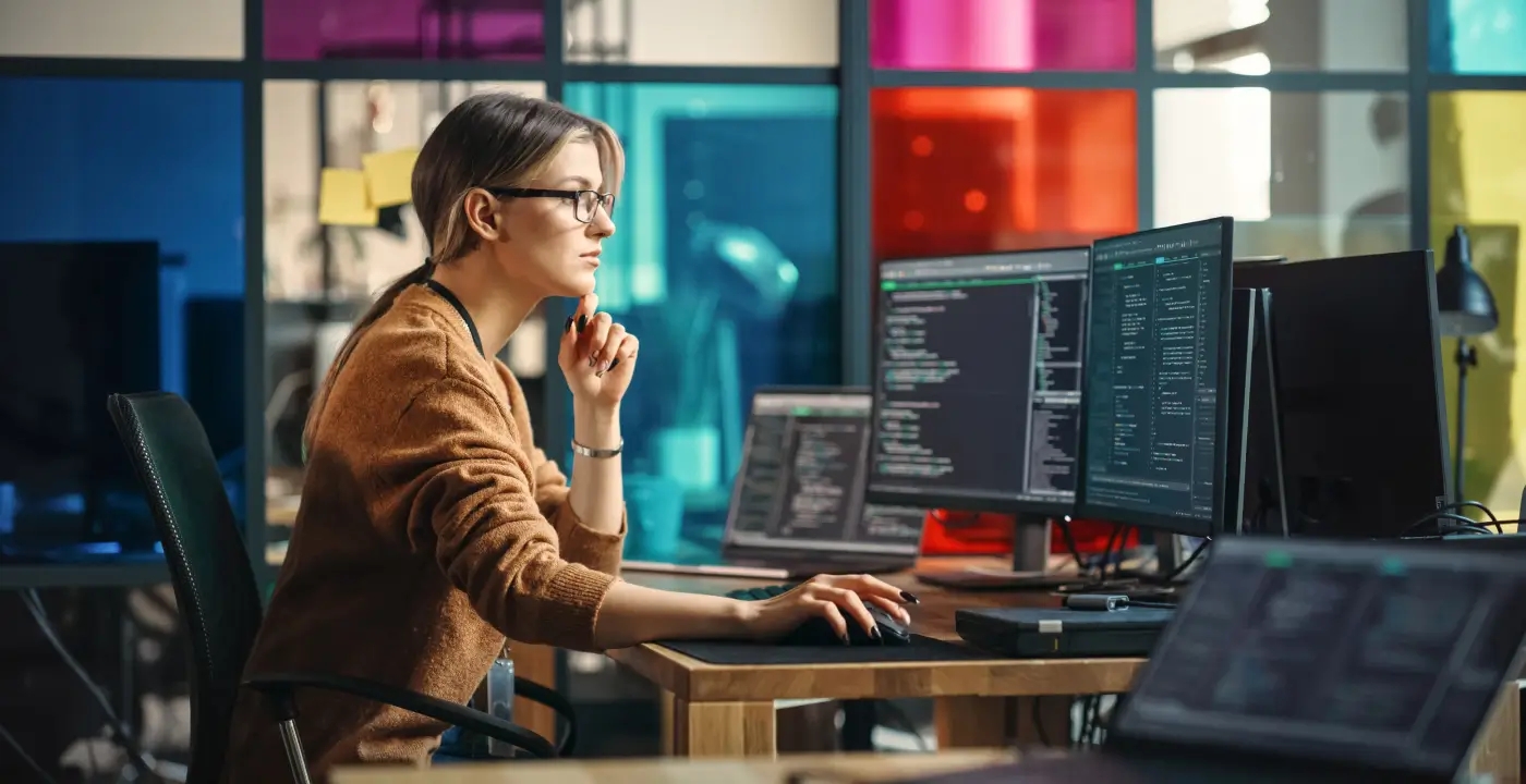 A woman sits at a computer, conducting on demand software testing services